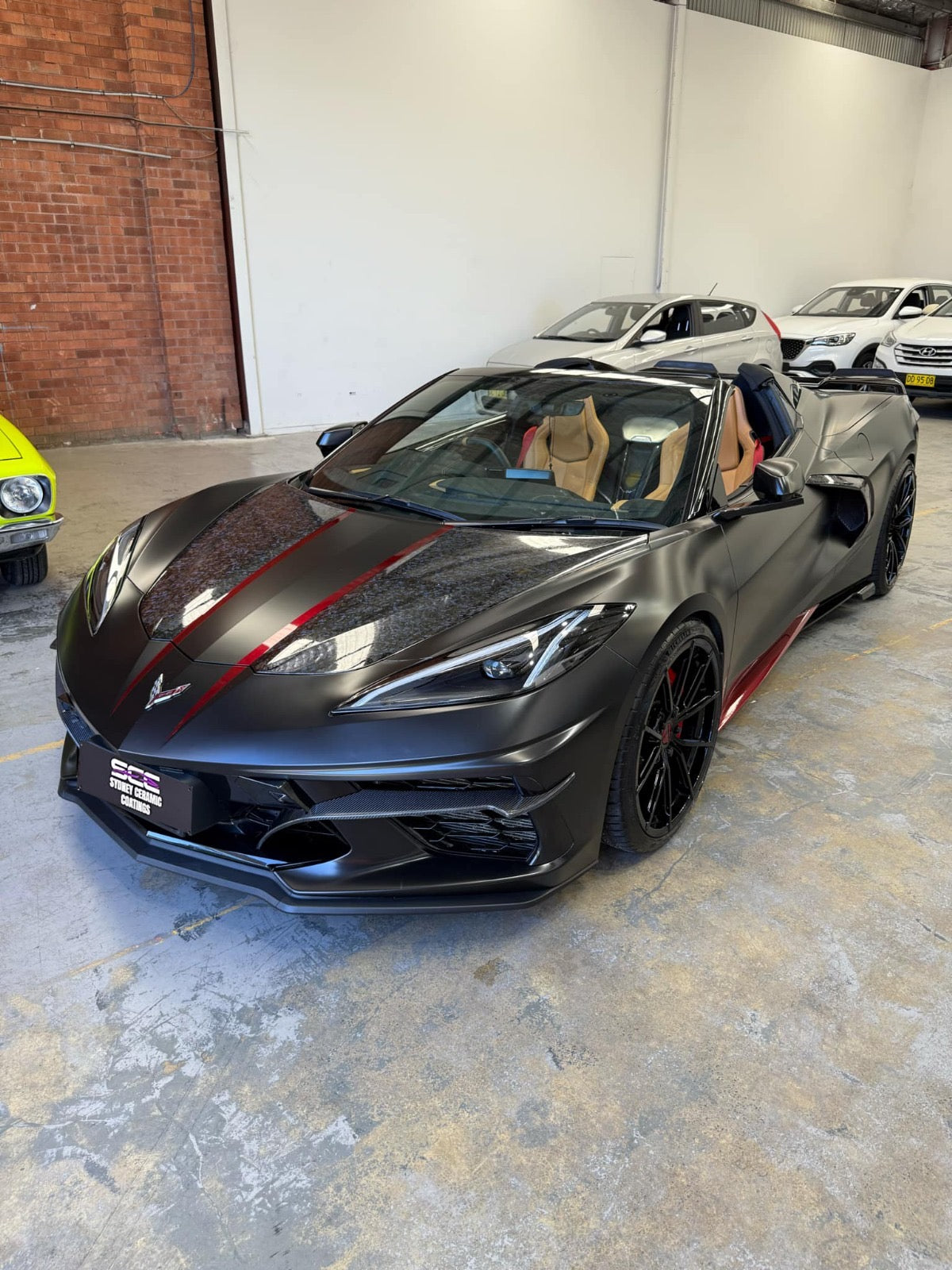 A black car with a ceramic coating parked indoors, with a red stripe design on the hood.
